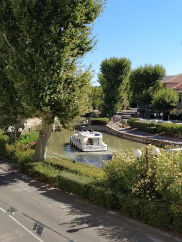 un bateau dans une rivière avec un arbre dans l'établissement Appartement avec balcon, bord du canal, Wifi., à Narbonne