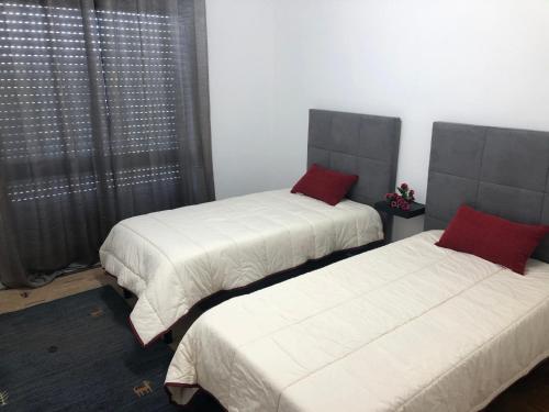 a bedroom with two beds with white sheets and red pillows at Apartamento Rio Minho in Vila Nova de Cerveira