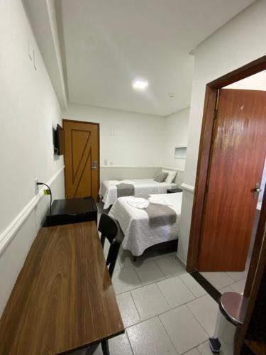 a room with a room with two beds and a table at Hotel Caiçara in Cachoeiro de Itapemirim