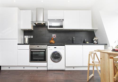 a kitchen with white cabinets and a washer and dryer at Holiday Lets London - I5 in London
