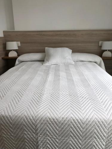 a bedroom with a large white bed with two lamps at Apartamentos Corcubión in Corcubión