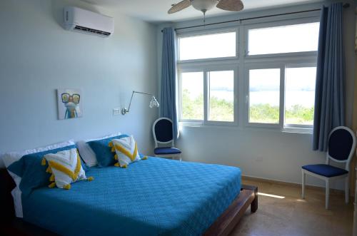1 dormitorio con 1 cama azul con 2 sillas y ventana en Casa Tanamera, en Boca Chica