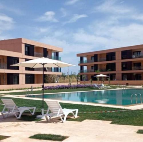 - une piscine avec des chaises et un parasol à côté d'un bâtiment dans l'établissement LDM Appartements Marrakech, à Marrakech