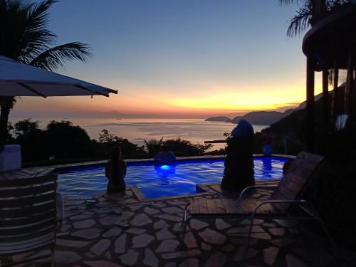 a group of people sitting around a swimming pool at sunset at Vila Lia in São Sebastião