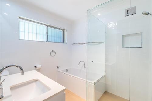 a white bathroom with a shower and a sink at 10 Garuwa Street - Fabulous Fingal Bay water views in Fingal Bay
