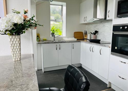 uma cozinha com armários brancos e um vaso de flores em Modern Upstairs Apartment in Dunedin Central em Dunedin