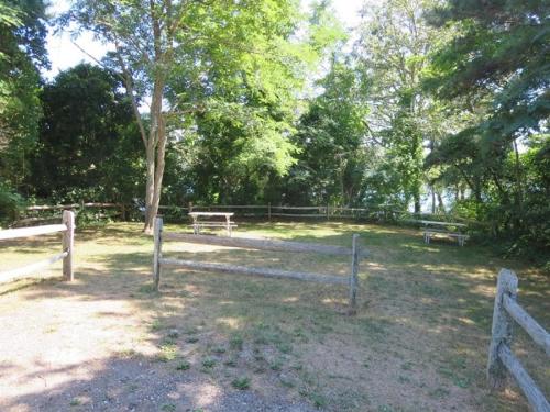 a fence with two benches in a field with trees at 151 Sky Way Chatham Cape Cod- -Cape Time in Chatham