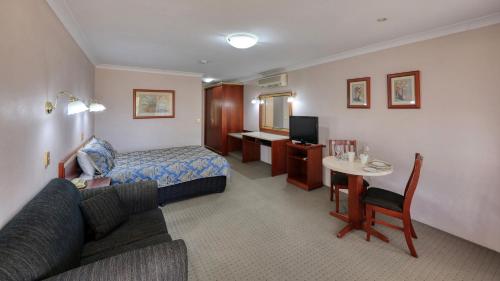 a hotel room with a couch and a bed and a table at Southern Comfort Motor Inn in Cootamundra