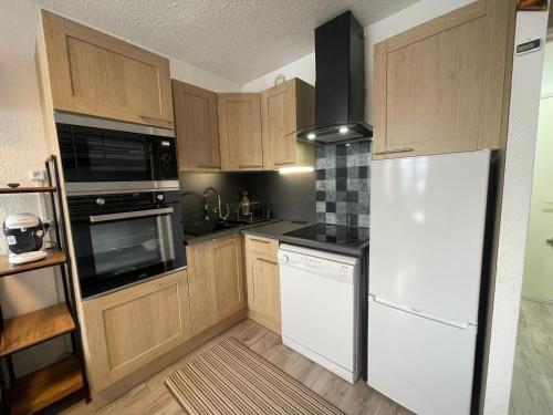 une cuisine avec des armoires en bois et un réfrigérateur blanc dans l'établissement Studio rénové avec accès direct aux pistes, bien équipé - FR-1-165A-169, à Enchastrayes