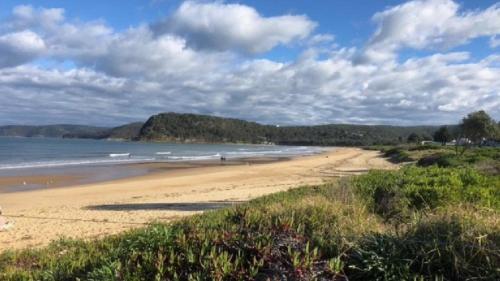 a beach with people walking on the sand at Mara Bello - Umina Beach in Umina