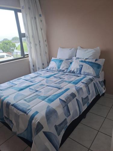 a bed with a blue and white comforter and a window at 3The Olive Complex Richards Bay 3900 in Richards Bay