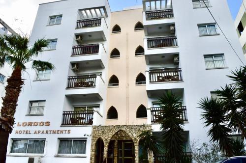 a white building with balconies and palm trees at Lordos Hotel Apartments Nicosia in Nicosia