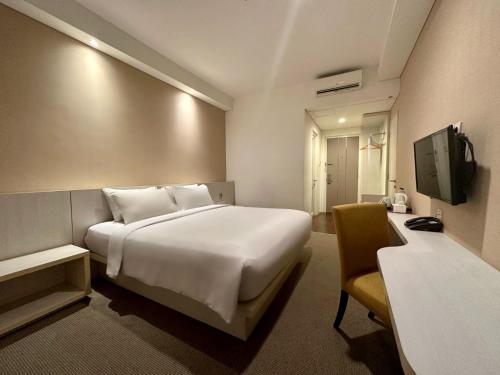 una habitación de hotel con una gran cama blanca y una silla en Yasmin Hotel Karawaci, en Tangerang