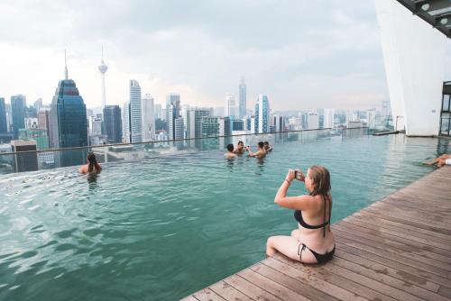 a woman taking a picture of people in a infinity pool at The Common Room @ Regalia in Kuala Lumpur
