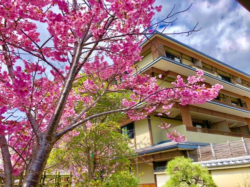 a tree with pink flowers in front of a building at Kadensho, Arashiyama Onsen, Kyoto - Kyoritsu Resort in Kyoto