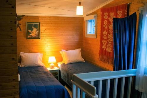 two beds in a room with wooden walls and blue curtains at Portaan Nahkurinverstas in Porras
