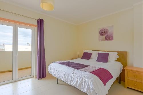 a bedroom with a bed with purple curtains and a window at Penthouse Papoila in Cabanas de Tavira