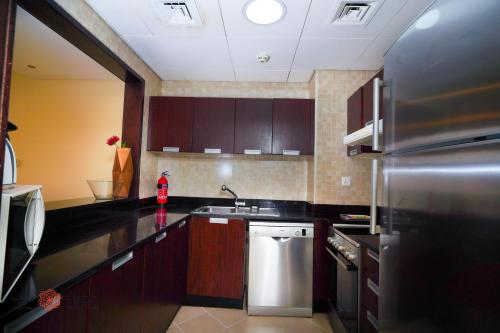 a kitchen with wooden cabinets and a stainless steel refrigerator at Alashrafia Saray, Lovely 2 BR apartment in Sport city in Dubai