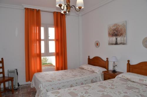 1 dormitorio con 2 camas y una ventana con cortinas de color naranja en Aptº ATALAYA , junto a la Playa, en Conil de la Frontera