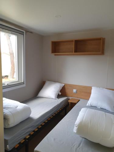 Duas camas num pequeno quarto com uma janela em Camping du Bois Dormant em Saint-Jean-de-Monts