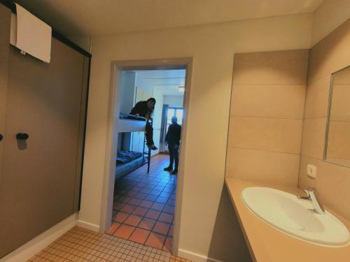 - un homme dans une salle de bains avec lavabo et miroir dans l'établissement Auberge de Jeunesse de Bouillon, à Bouillon