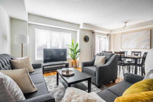 a living room with couches and a television and a table at New 3BR Townhouse, Minutes to Niagara Falls and Brock University by GLOBALSTAY in Thorold