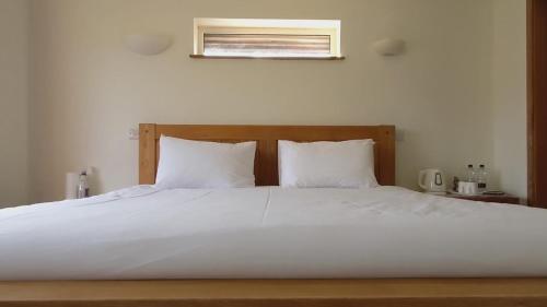 a large white bed with white sheets and a window at Blackhouse Bothies in Balallan