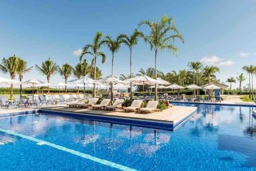 una piscina con sillas, sombrillas y palmeras en Linda Casa de Campo Nova em condomínio, en Porangaba