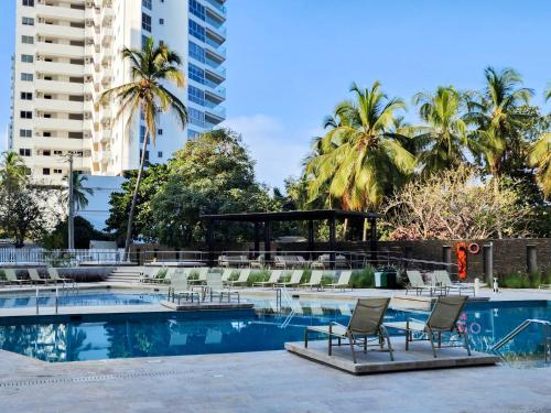 una piscina con sillas, palmeras y edificios en Apartamentos en Reserva del Mar - By BEDVIAJES, en Santa Marta