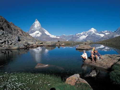 three people sitting on rocks near a lake with a mountain at Apartment Breithorn by Interhome in Zermatt