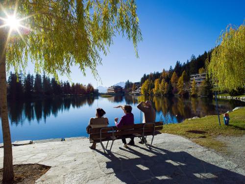 three people sitting on a bench near a lake at Apartment Victoria B 7 by Interhome in Crans-Montana