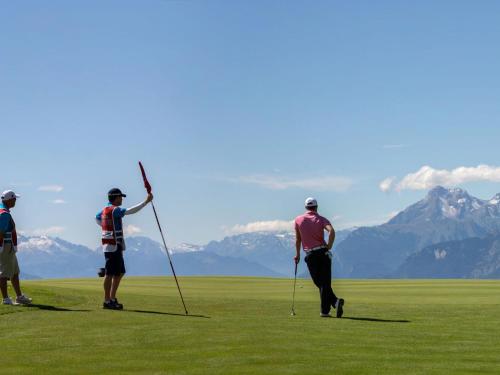 three people playing golf in a field with mountains in the background at Apartment Clair-Azur B 65 by Interhome in Randogne