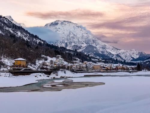 a snowy mountain with a town next to a river at Apartment Albergo Diffuso - Cjasa Ustin-3 by Interhome in Barcis