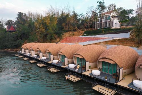 a row of thatched cottages on the water at VeeVaree Riverkwai Resort in Ban Kaeng Raboet