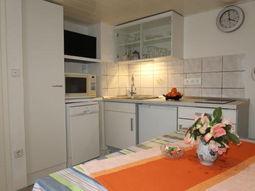 una cocina con armarios blancos y una mesa con flores. en Apartment Osterende-1 by Interhome, en Süderwisch