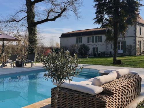 - une piscine avec un canapé en osier à côté d'une maison dans l'établissement Moulin de La Vergnotte, à Saint-Antoine-de-Breuilh