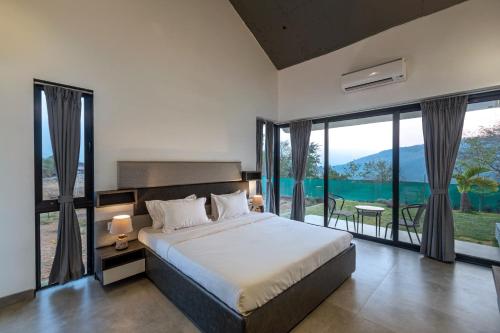 a bedroom with a large bed and large windows at SaffronStays Stargazer, Karjat - luxury pool villa with lake view in Karjat