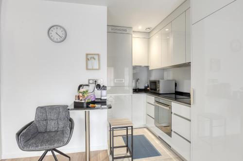 une cuisine avec des placards blancs, une chaise et un réveil dans l'établissement L'escale Parisienne - METRO 3 min, Proche JO, Direct au Louvre,Galeries Lafayette, Opéra,, à Aubervilliers