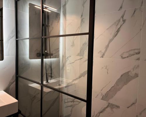 La salle de bains est pourvue d'une douche en verre avec des murs en marbre. dans l'établissement Hôtel La Pièce, à Bruxelles