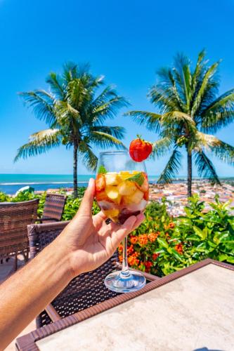 a person holding a drink in front of the beach at Porto Seguro Eco Bahia Hotel in Porto Seguro