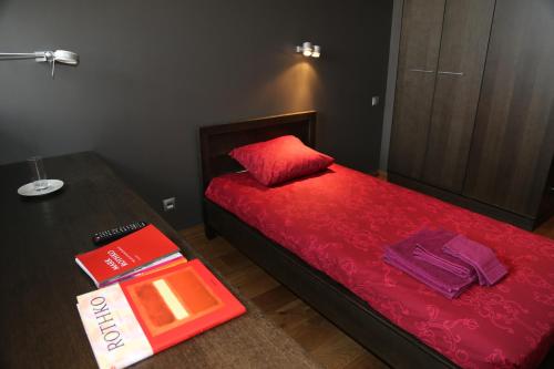 a bedroom with a red bed with a table and a book at Rothko Museum residences in Daugavpils