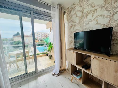 a living room with a flat screen tv and a balcony at LES PALMIERS - Appartement avec piscine proche plage in Antibes