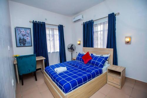 Schlafzimmer mit einem blauen Bett, einem Schreibtisch und einem Fenster in der Unterkunft AJI Warm 2BED Apartment (Ijegun, Lagos) in Lagos