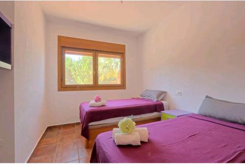 Habitación con 2 camas con sábanas moradas y ventana. en Villa Jacinta, en Asprillas