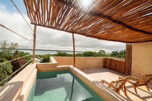 a swimming pool with two chairs and a straw umbrella at Bacalari Hotel Boutique in Bacalar
