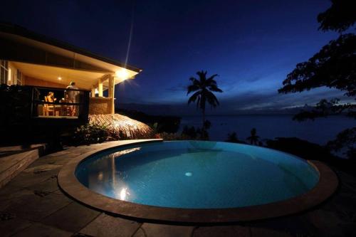 a swimming pool in front of a house at night at Beachfront Villa - House of Bamboo, Infinity Pool in Savusavu