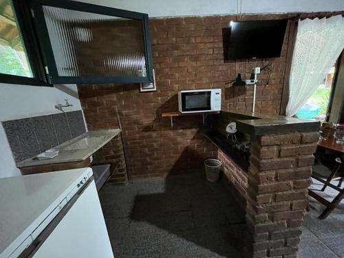 uma cozinha com uma televisão e uma parede de tijolos em Sitio Serenar Chalés Equipados em Penedo
