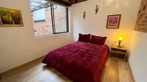 1 dormitorio con 1 cama con colcha roja y ventana en Las Aguas Inn, en Bogotá