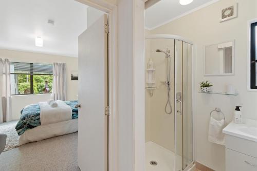 baño blanco con ducha y cama en Riverside Accommodation en Karangahake