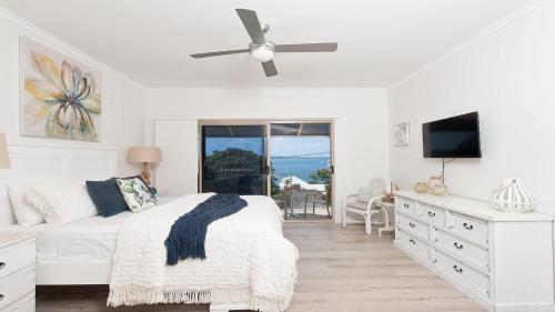 a white bedroom with a bed and a ceiling fan at Dutchie's Sand & Sea Beach House - easy walk to the beach in Nelson Bay